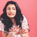 Ragazza con i capelli neri lunghi con espressione di disgusto e mani che sembrano allontanare qualcosa vicino a lei